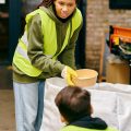 A woman wearing a vibrant yellow jacket, participating in recycling by holding a bowl.